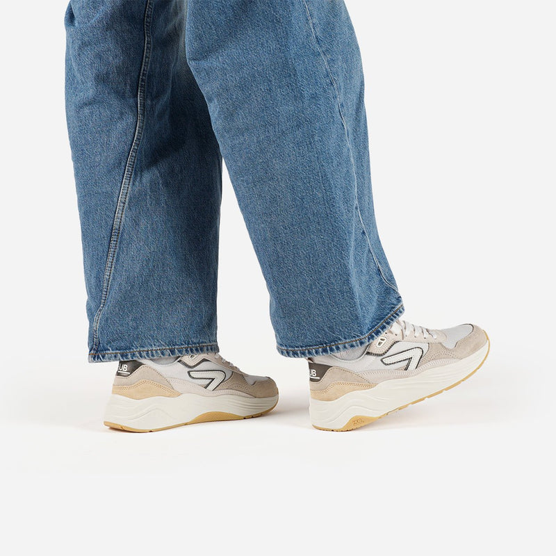 Person wearing blue jeans and beige HUB sneakers on a white background