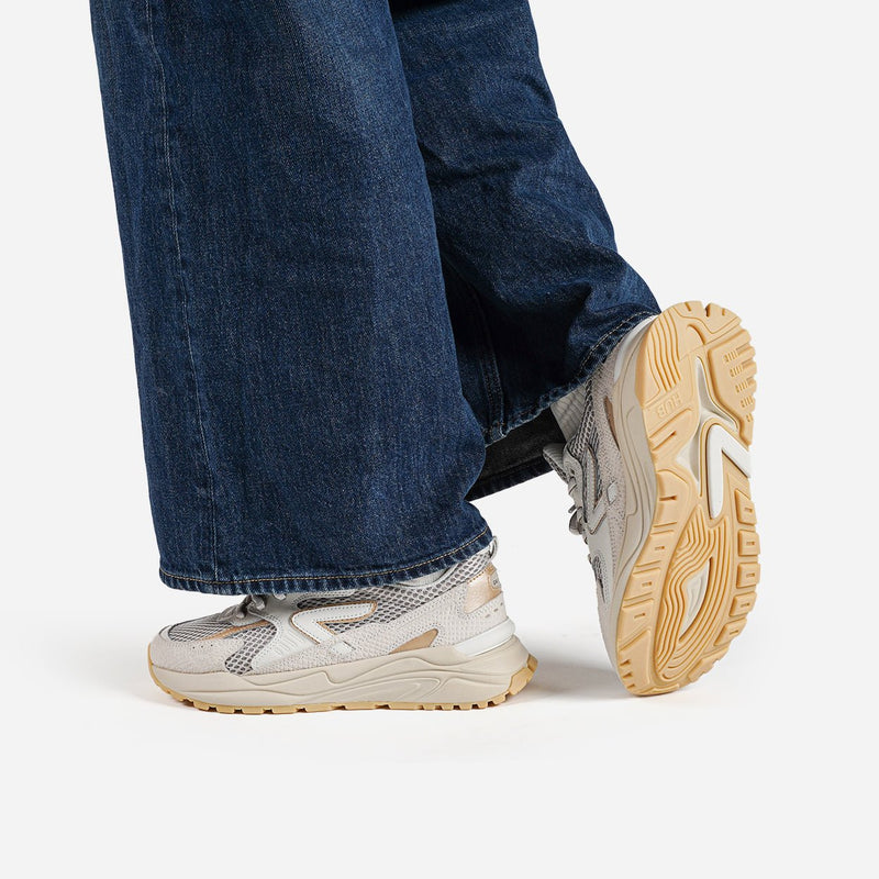 Close-up of a person wearing blue jeans and beige snake HUB sneakers with gum soles on a white background