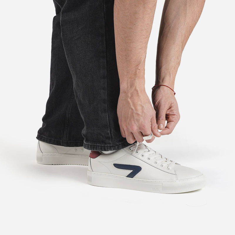 Person wearing white HUB sneakers with a blue logo on a white background